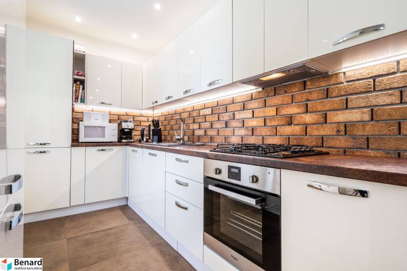 Kuchyně ve 3-pokojovém bytě, s cihlovou stěnou a moderními spotřebiči.