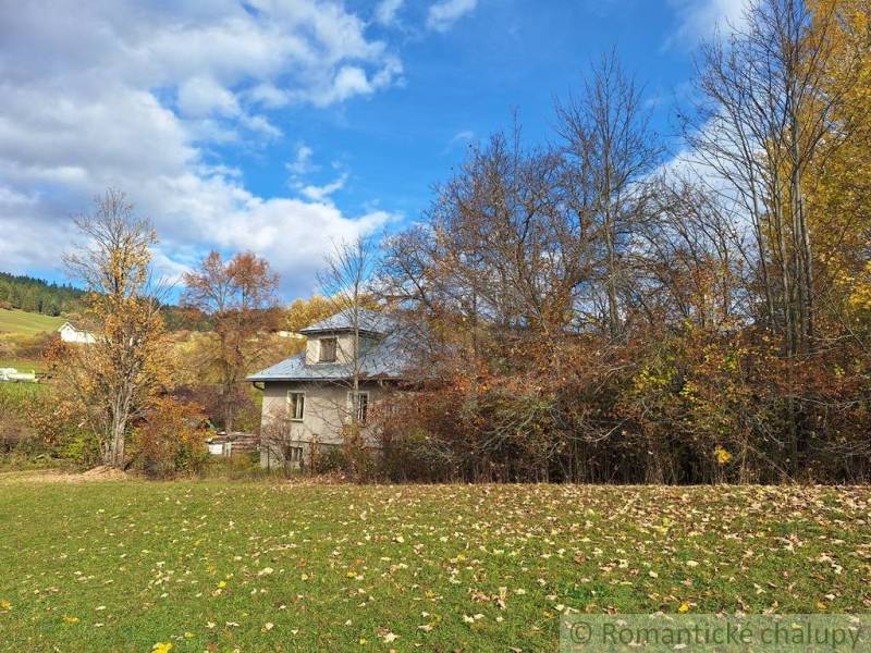 Rodinný dům v Liptovských Beharovcích obklopený podzimními stromy a zelenou loukou.