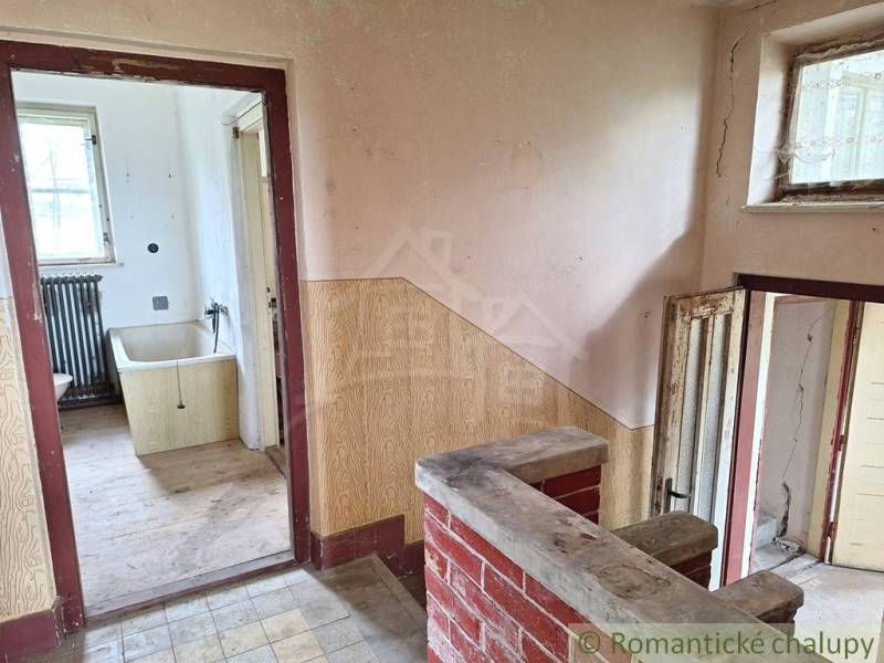 Interiér rodinného domu s obkladem, starou vanou a podlahou s dřevěným dekorem.