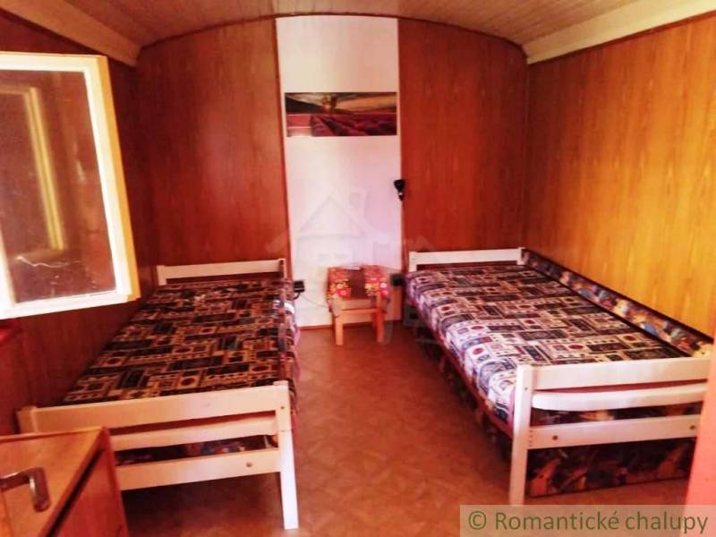 Dřevěný interiér chaty s dvěma lůžky a podlahou s dřevěným dekorem.