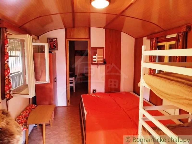 Interiér chaty s poschoďovou postelí, podlahou s dřevěným dekorem a otevřeným oknem.