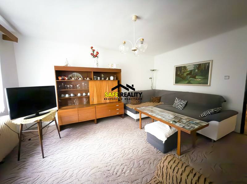 Obývací pokoj v rodinném domě s pohovkou, televizorem a dřevěnou obývací stěnou.