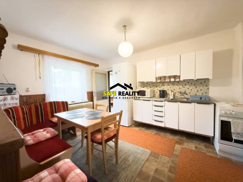 Kuchyně v rodinném domě se světlým nábytkem, jídelním stolem a posezením.