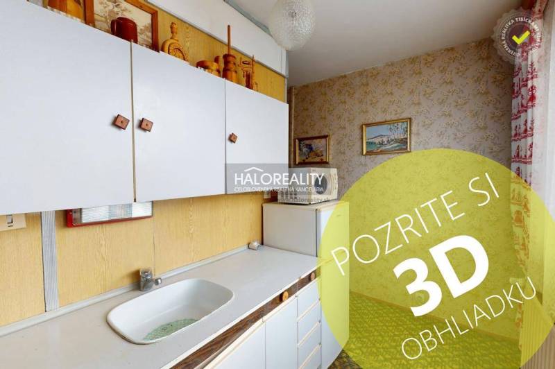 Kuchyně ve 3-pokojovém bytě s bílými skříňkami a obrázky na stěnách.