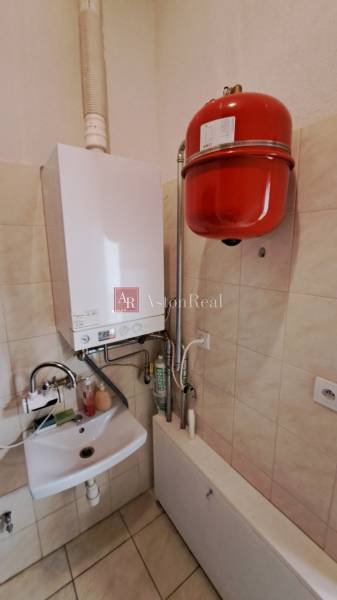 Plynový kotel s umyvadlem v obchodních prostorách, dlažba, stěny obložené dlaždicemi.