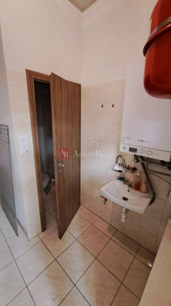 Koupelna v obchodních prostorách s umyvadlem, bojlerem a dveřmi na toaletu.