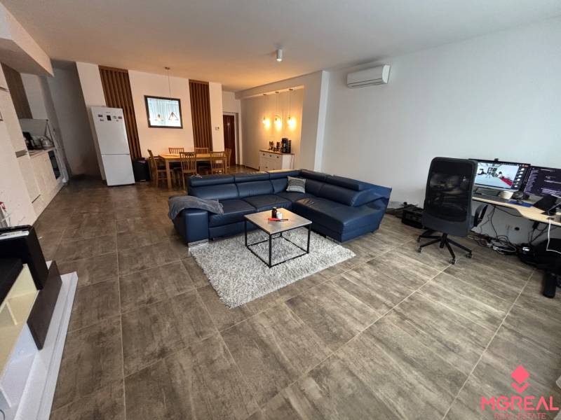 Obývací pokoj v dvoupokojovém bytě s modrou sedačkou a pracovním stolem.