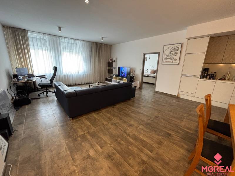 Obývací pokoj dvoupokojového bytu s tmavou pohovkou a pracovním koutem.