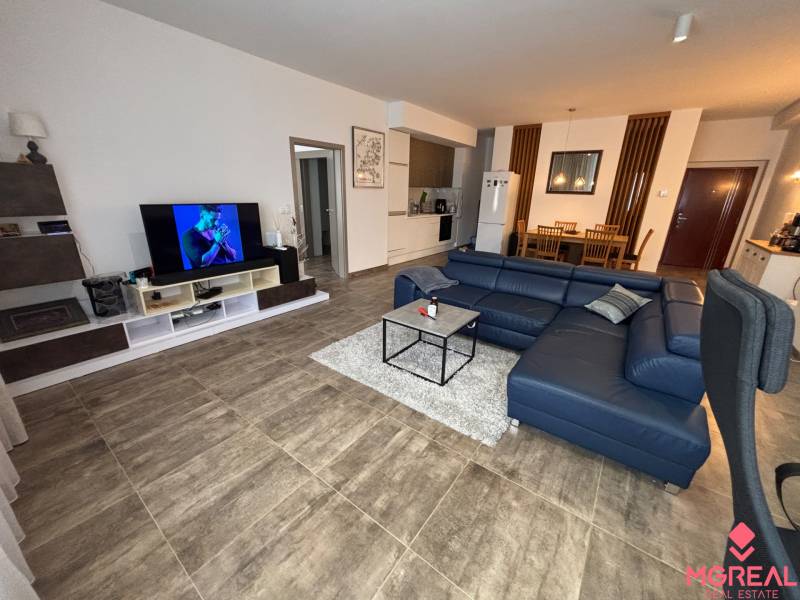 Obývací pokoj v 2-pokojovém bytě s tmavou sedačkou a televizorem, podlaha s dřevěným dekorem.