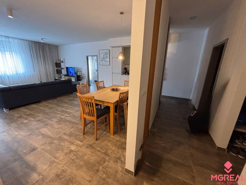 Jídelní stůl s dřevěnými židlemi v 2-pokojovém bytě. Součástí je pohovka a televizor.