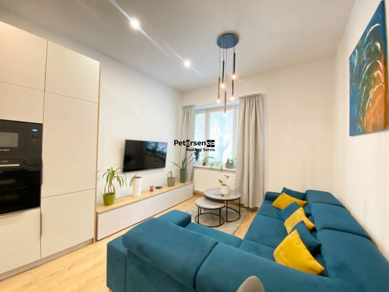 Obývací pokoj v 2-pokojovém bytě s modrou sedačkou a podlahou s dřevěným dekorem.