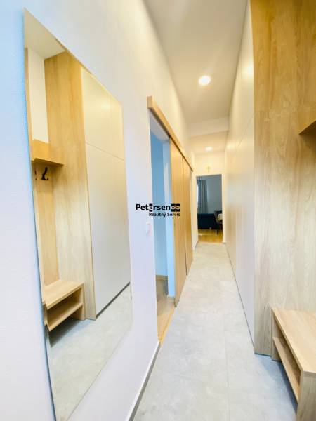 Chodba s podlahou s dřevěným dekorem v 2-pokojovém bytě, skříněmi a zrcadlem.