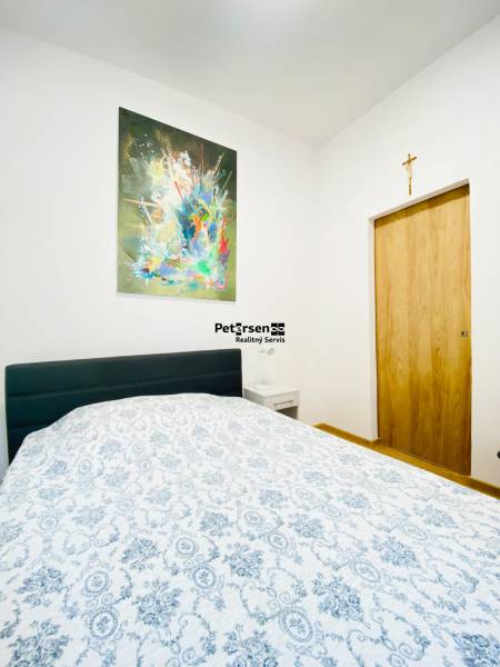 Ložnice s obrazem na stěně, postelí a nočním stolkem v dvoupokojovém bytě.