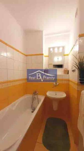 Koupelna v 2-pokojovém bytě s obkladem v teplých odstínech a vanou.