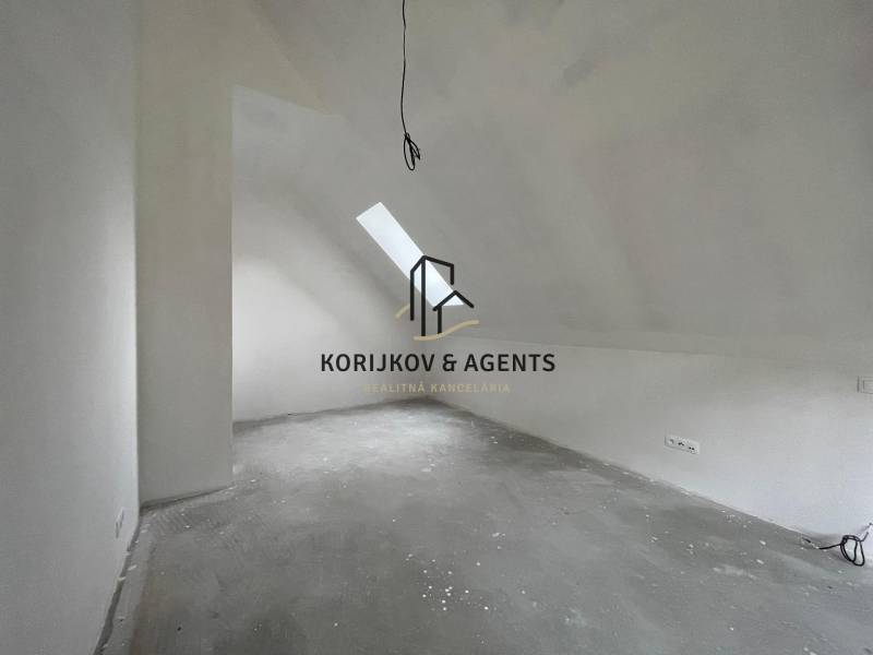 Podkrovní místnost v rodinném domě s oknem na stropě a elektrickými zásuvkami.