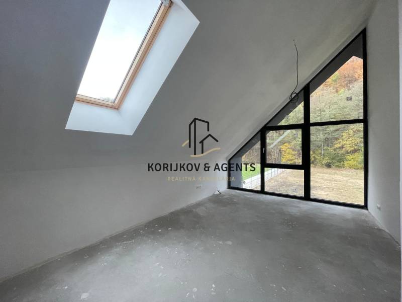 Podkrovní pokoj v rodinném domě s velkými okny a výhledem na les.