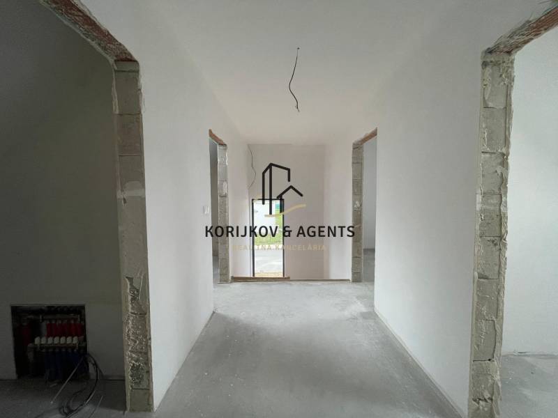 Interiér rodinného domu s bílými stěnami a otevřenými dveřmi do další místnosti.