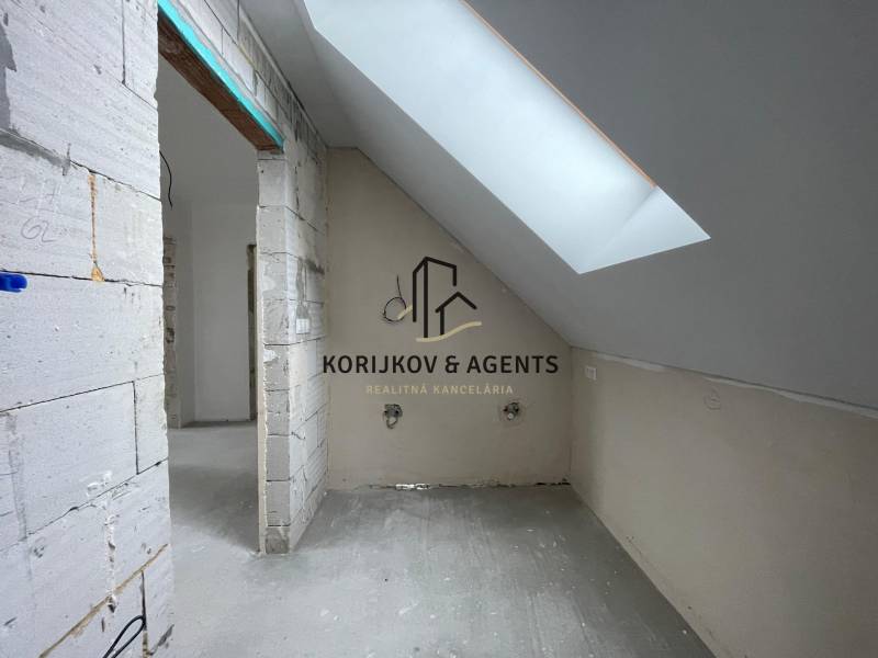 Podkrovní místnost v rodinném domě, se střešním oknem a nedokončenými stěnami.