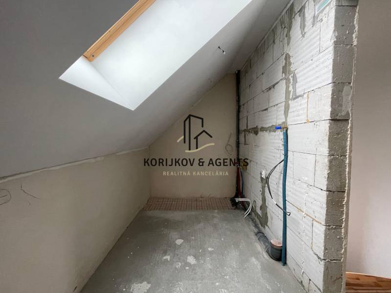 Podkrovní prostor rodinného domu s betonovou podlahou a střešním oknem.