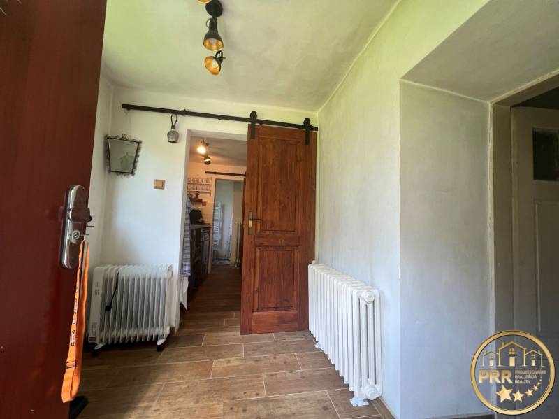 Interiér chaty s podlahou s dřevěným dekorem, radiátorem a posuvnými dřevěnými dveřmi.