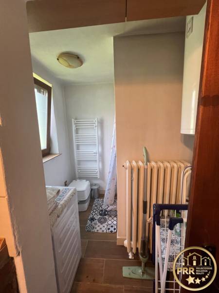 Malá koupelna s pračkou, radiátorem a toaletou, vhodná pro chatu.