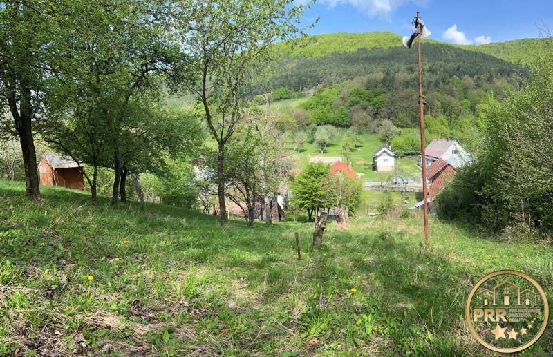 Krásná přírodní scenérie s chatou, stromy a malebnou vesničkou na pozadí kotliny.