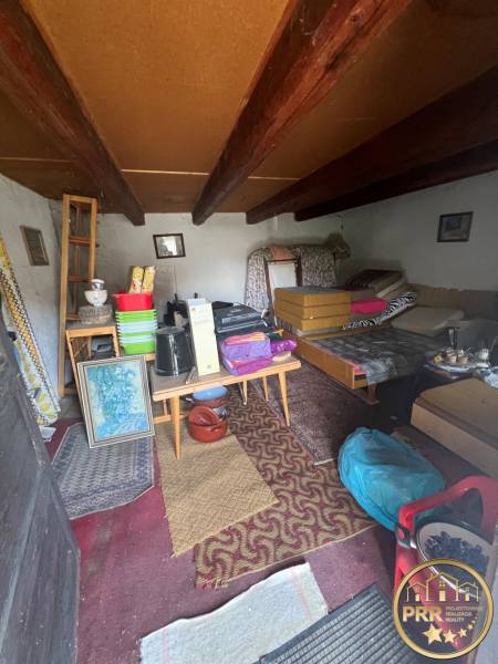 Interiér nepoužívané chaty s venkovským nábytkem a stropními trámy.