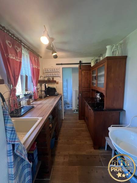 Kuchyně v dřevěné chatě s rustikálním nábytkem, umyvadlem a dekorativními záclonami.