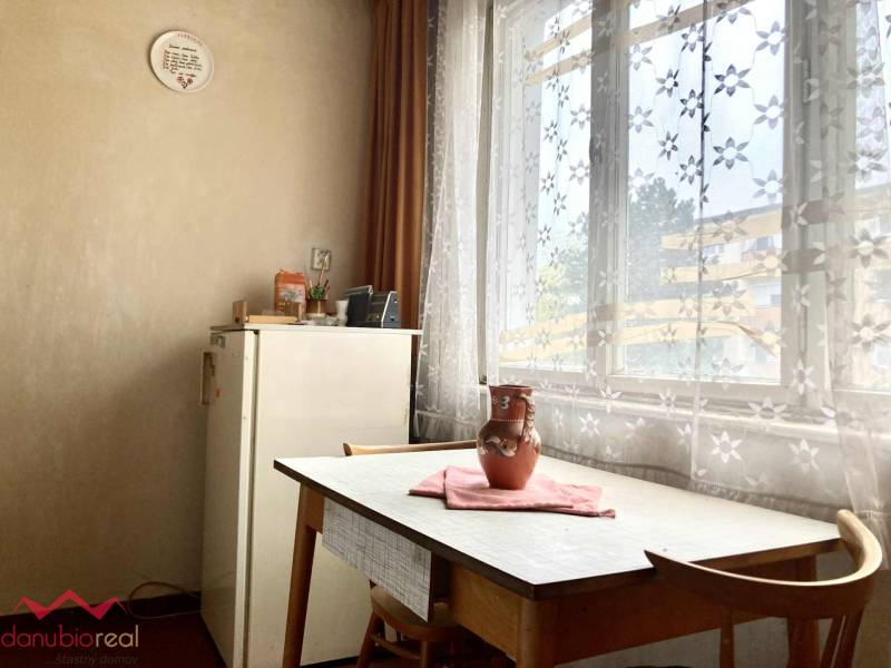 Jídelna ve 3-pokojovém bytě se stolem, židlemi a záclonami s květinovým vzorem.