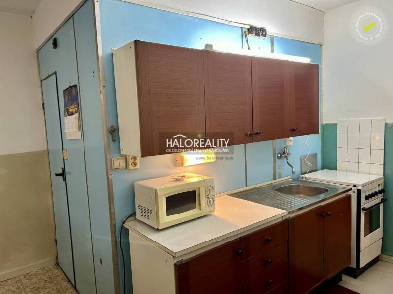 Kuchyně se staršími skříňkami, mikrovlnkou a sporákem ve 4-pokojovém bytě.