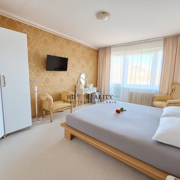 Ložnice v 3-pokojovém bytě s elegantním nábytkem, zlatou tapetou a bílým kobercem.