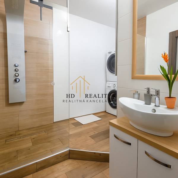 Koupelna v 3-pokojovém bytě s umyvadlem, sprchovým koutem a pračkou, s podlahou s dřevěným dekorem.