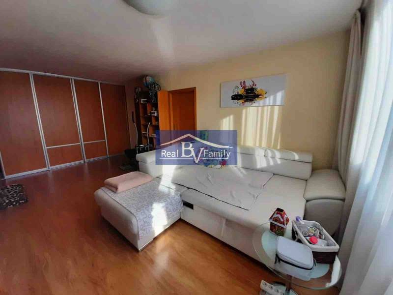 Světlý obývací pokoj v 2-pokojovém bytě s podlahou s dřevěným dekorem a bílou sedačkou.