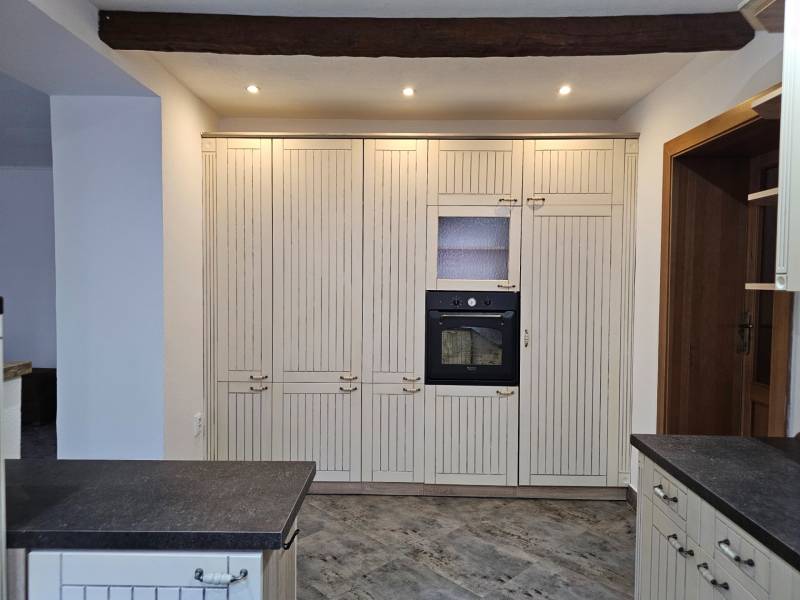 Kuchyně s tmavou pracovní deskou a vestavěnou troubou, podlaha s dřevěným dekorem.