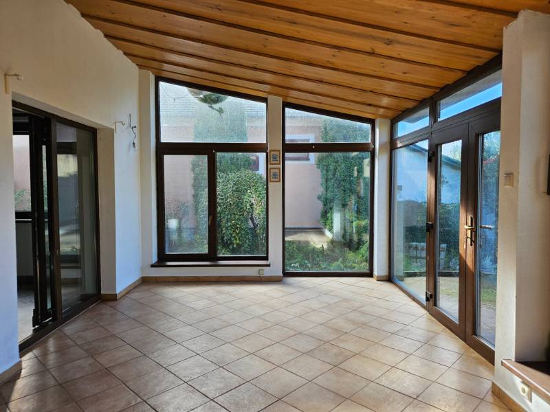 Pokoj v rodinném domě s velkými okny a dlažbou, výhled do zahrady.