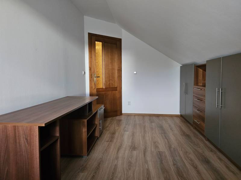 Pokoj v rodinném domě s nábytkem, bílými stěnami a podlahou s dřevěným dekorem.