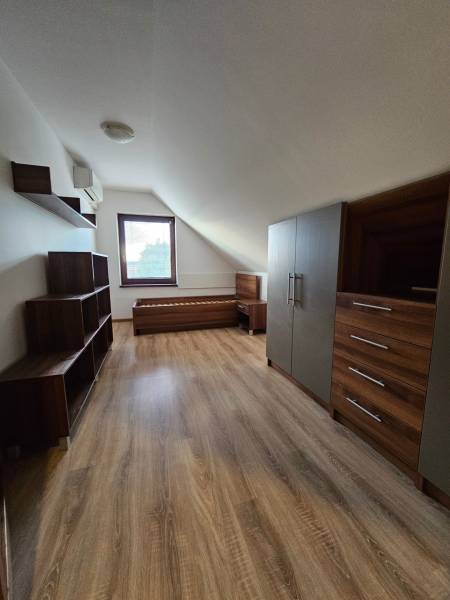 Podkroví rodinného domu s nábytkem, podlahou s dřevěným dekorem a oknem.