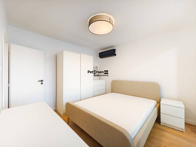 Ložnice v 2pokojovém bytě s postelí, skříní, komodou a podlahou s dřevěným dekorem.