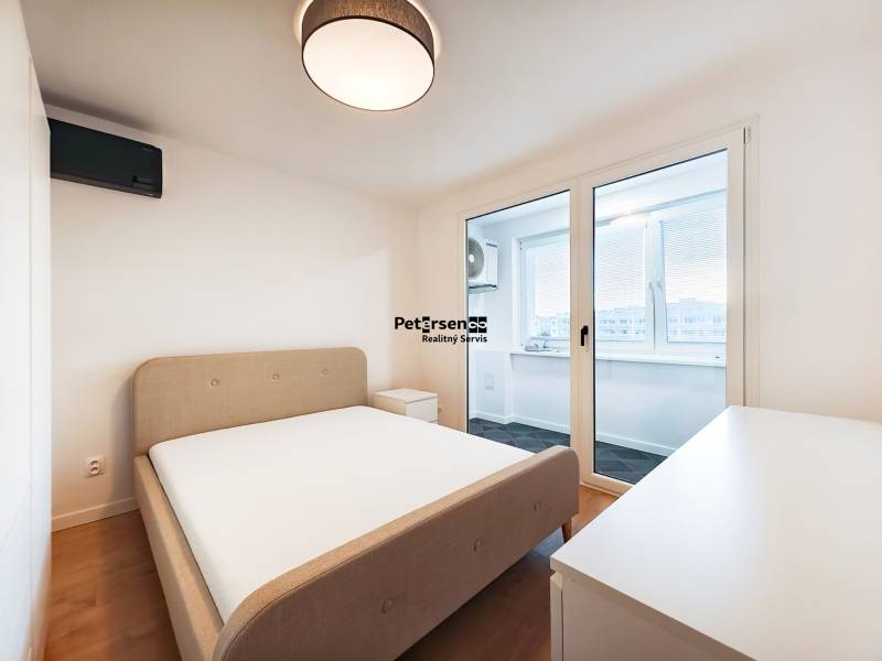 Ložnice v 2-pokojovém bytě s postelí, stolkem a balkonem, podlaha s dřevěným dekorem.