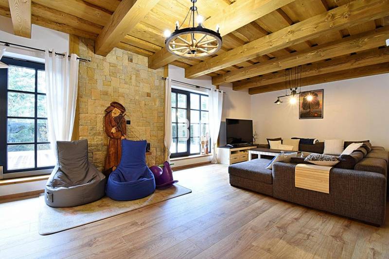 Interiér chaty s kamennou stěnou, velkou pohovkou a podlahou s dřevěným dekorem.