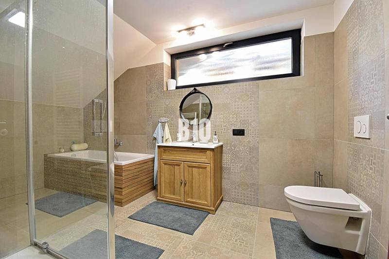 Koupelna s vanou, sprchou, zrcadlem a skříňkou v chatě. Světlé obklady a dlažba.