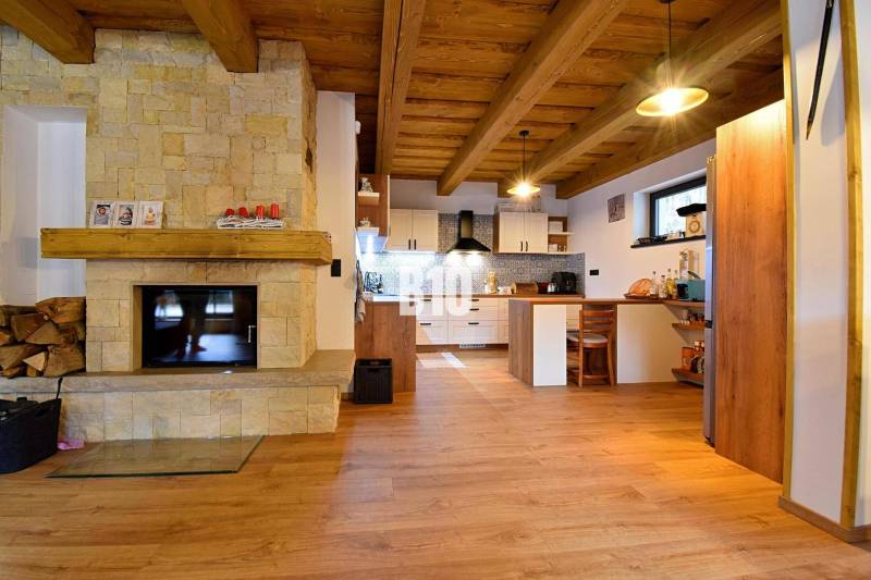 Interiér chaty s kachlovými kamny, dřevěným stropem a podlahou s dřevěným dekorem.