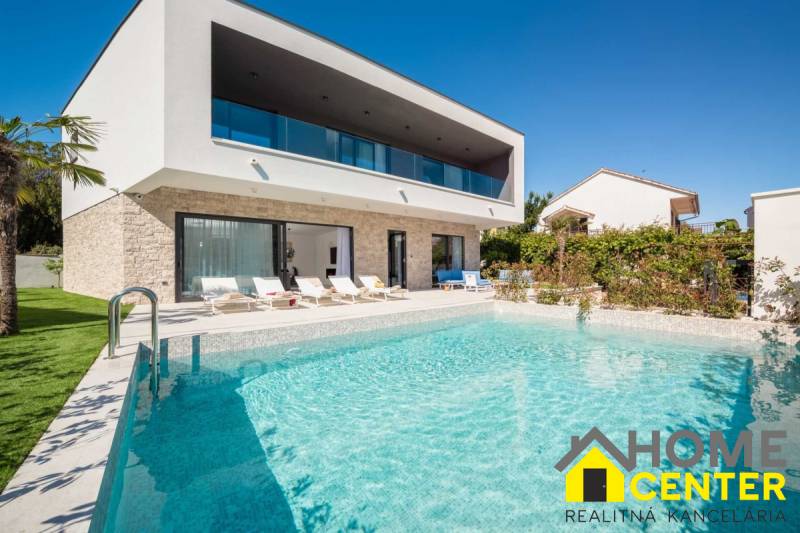 Vila v Bale s bazénem a lehátky, obklopená zelení a modrou oblohou.