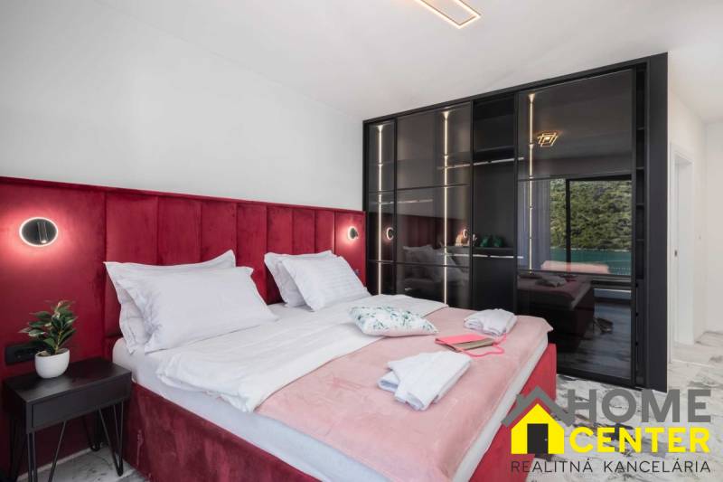 Ložnice ve vile s postelí čalouněnou červeným sametem a skleněnou skříní.