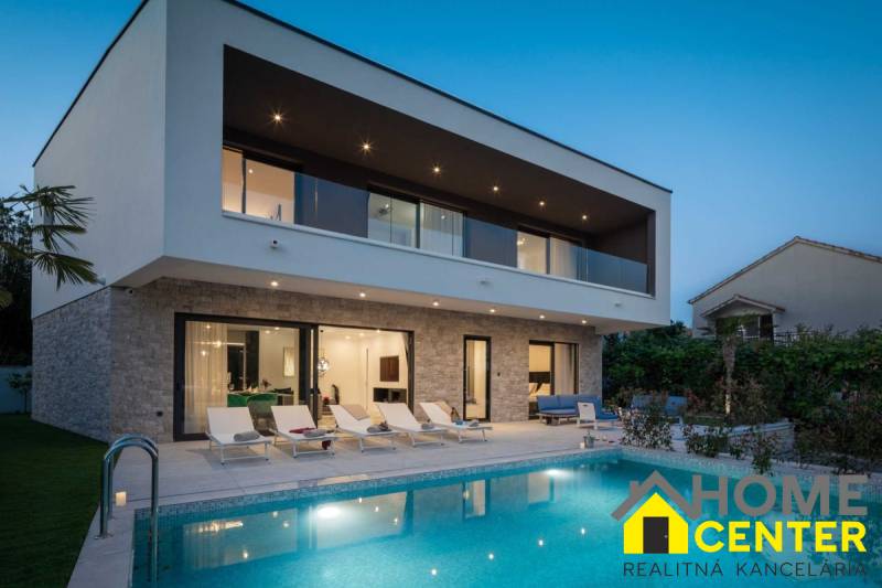 Vila v Balích s bazénem, lehátky a terasou během soumraku.