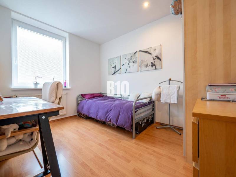 Ložnice ve 4pokojovém bytě s podlahou s dřevěným dekorem a fialovým přehozem.