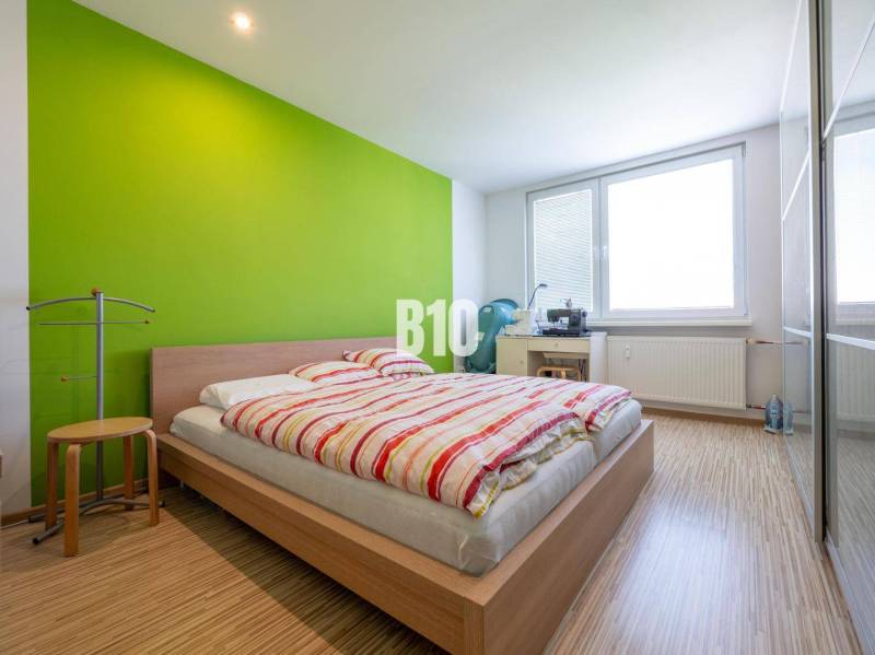 Ložnice ve 4pokojovém bytě s podlahou s dřevěným dekorem a zelenou stěnou.