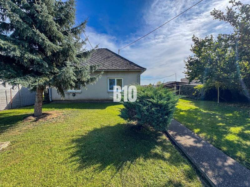 Rodinný dům v Ondřejovcích s travnatou zahradou, dvěma stromy a keřem u chodníku.