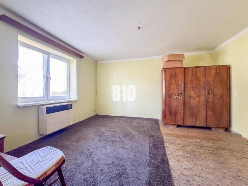 Pokoj v rodinném domě s kobercem, starou skříní a křeslem.