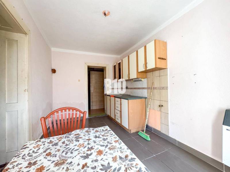 Kuchyně s jednoduchými skříňkami, kachličkami a stolem v rodinném domě.